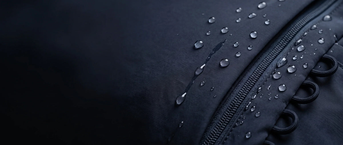 Rain beading on the water-repellent nylon shell of a hybeks Drift bag in Midnight Transit, the surface behaviour a careful hand wash preserves