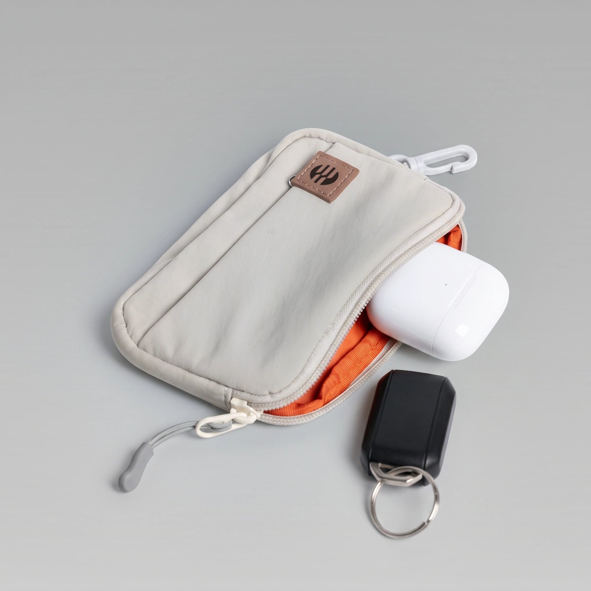 hybeks Drift Kit in Morning Fog, unzipped, showing the orange lining, with earbuds and a key tracker.